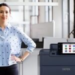 Una mujer de pie junto a la impresora Xerox® PrimeLink® Serie C9200 en un entorno de oficina moderno