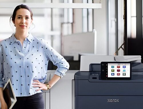 Una mujer de pie junto a la impresora Xerox® PrimeLink® Serie C9200 en un entorno de oficina moderno